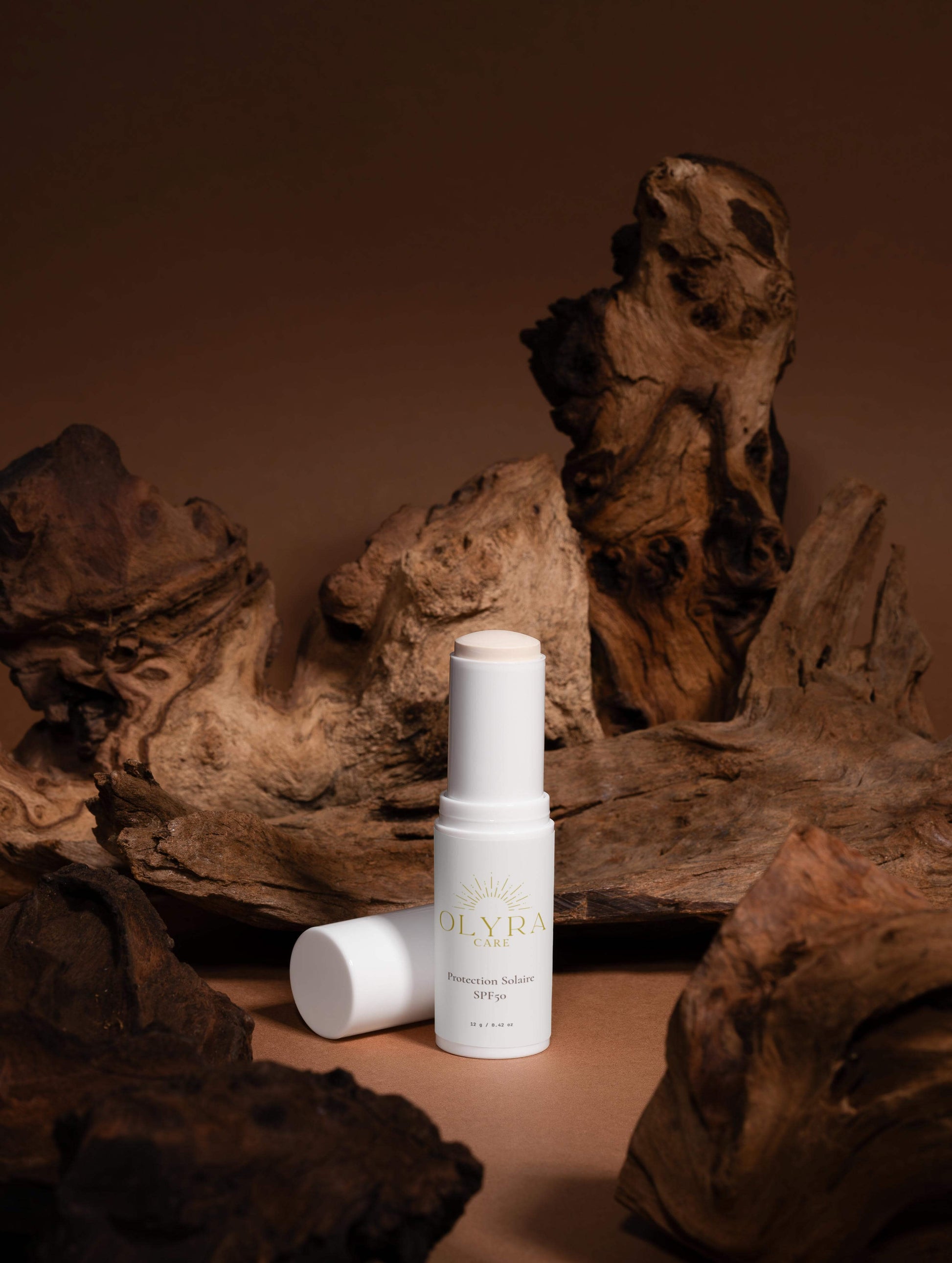 Protection solaire visage SPF50 en stick Olyra Care sur fond naturel en bois.