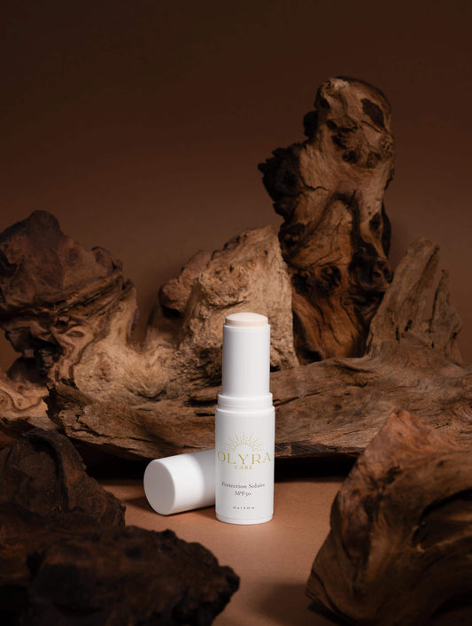 Protection solaire visage SPF50 en stick Olyra Care sur fond naturel en bois.